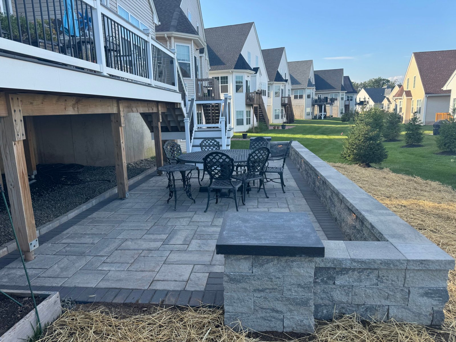 Patio area featuring a stone wall and metal dining set, surrounded by landscaped yard and residential homes, highlighting Urban Landscapes' outdoor living space design services.
