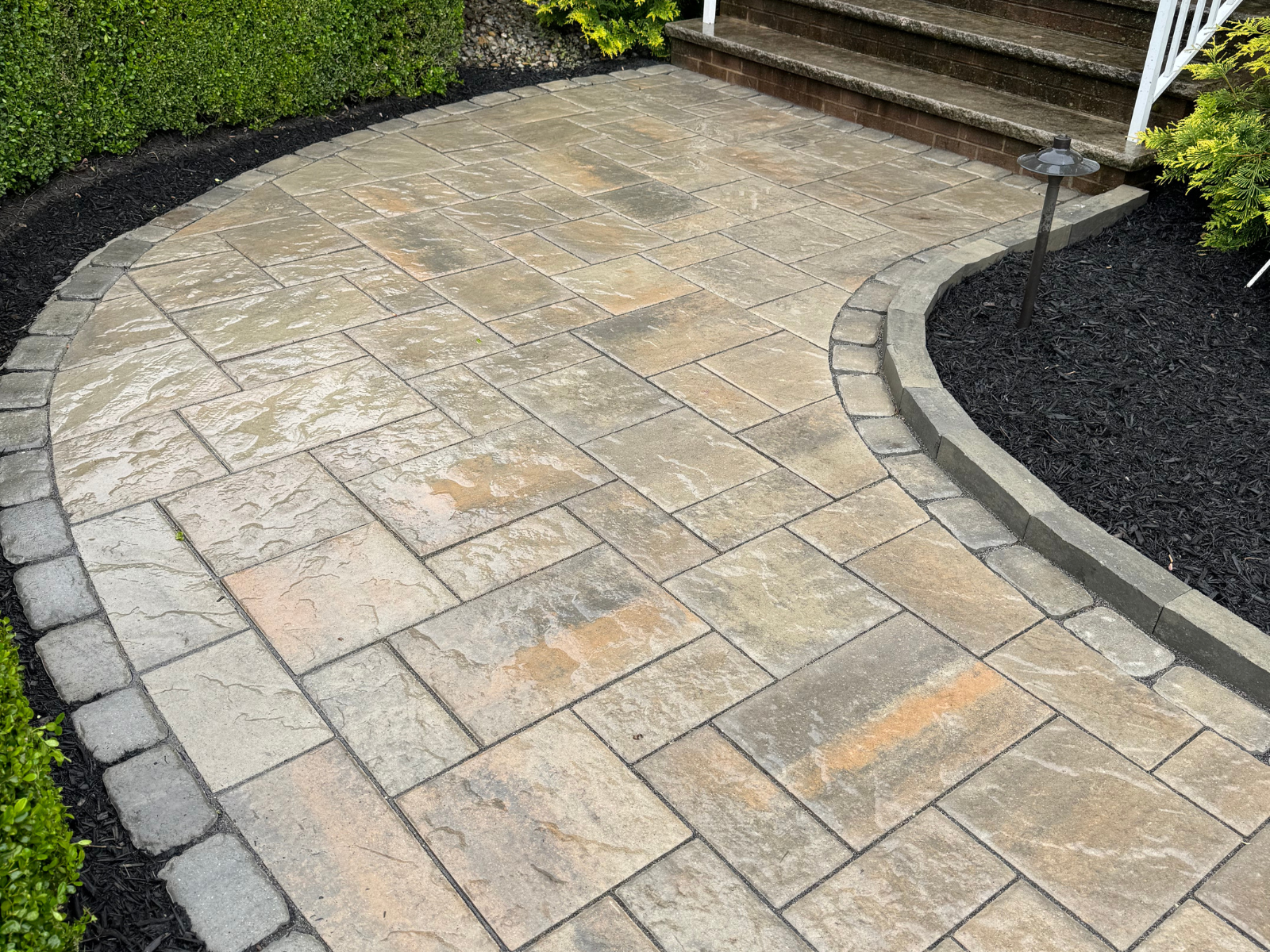 Paved walkway with a curved design, featuring textured stones, bordered by black mulch and greenery, creating a safe and aesthetically pleasing path for outdoor spaces.