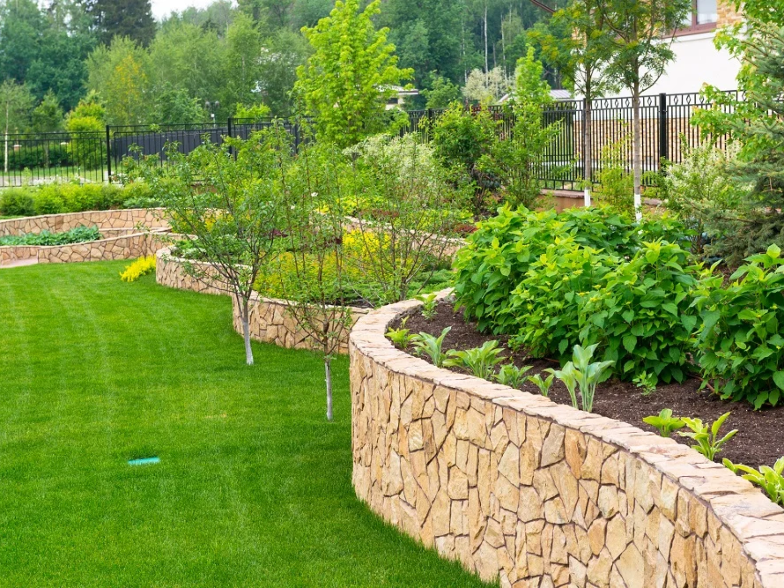 Lush landscaped garden with stone retaining walls, featuring vibrant greenery and well-maintained flower beds, illustrating seasonal cleanup and maintenance services by Urban Landscapes.