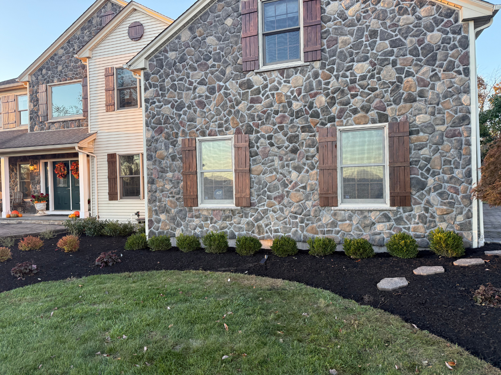 Stone exterior of a home with evergreen shrubs and mulch, showcasing professional landscaping and shrub maintenance by Urban Landscapes.