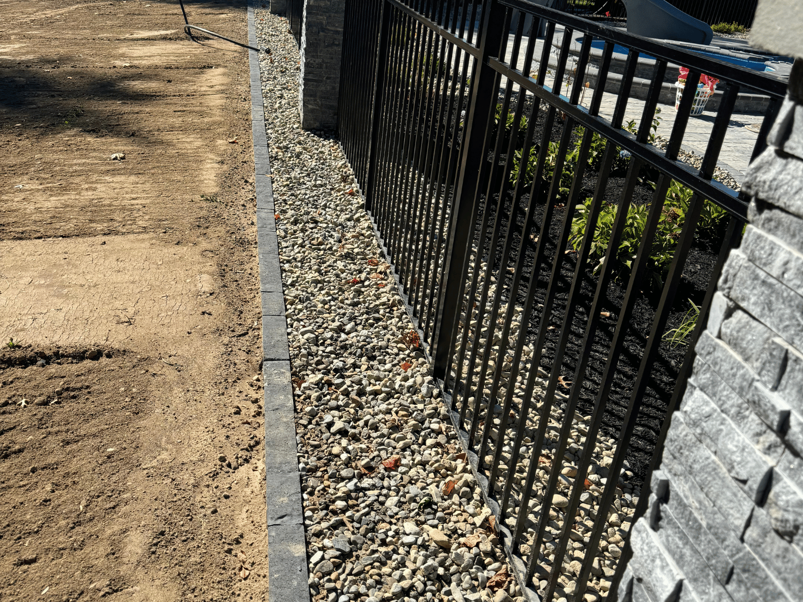 Aluminum fencing installed along a landscaped area with gravel, showcasing proper installation techniques and adherence to ground irregularities.