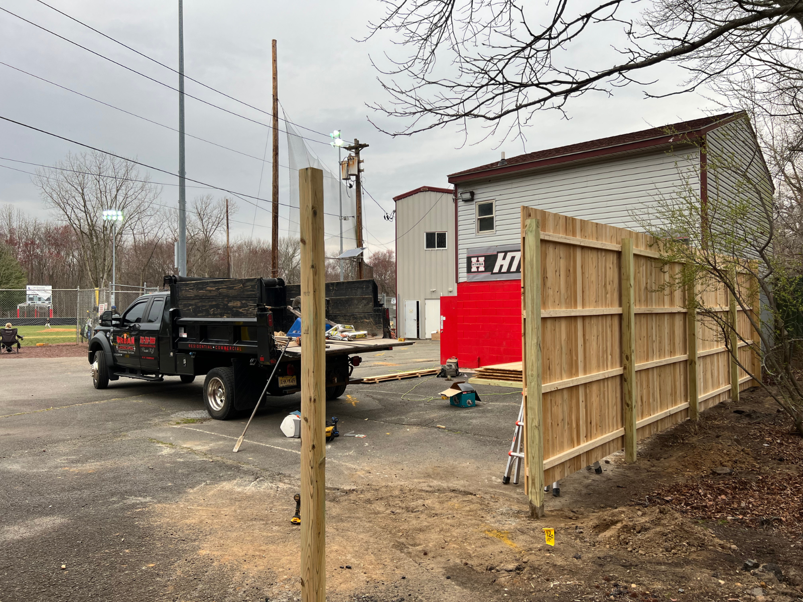 Wood fencing installation in progress, featuring treated pine boards and a work truck, with a sports facility in the background, emphasizing quality craftsmanship and maintenance.