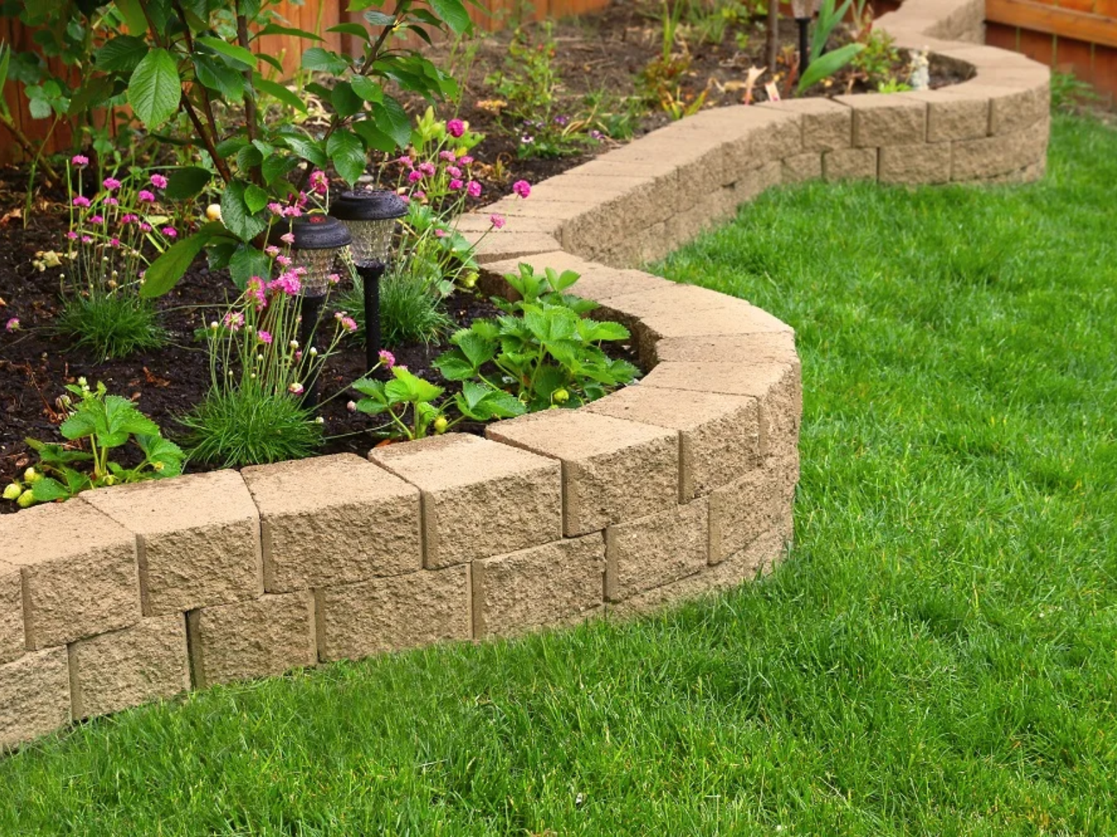 Curved stone garden border with colorful flowers and green plants, enhancing a well-maintained landscape, reflecting Urban Landscapes' property revitalization services.