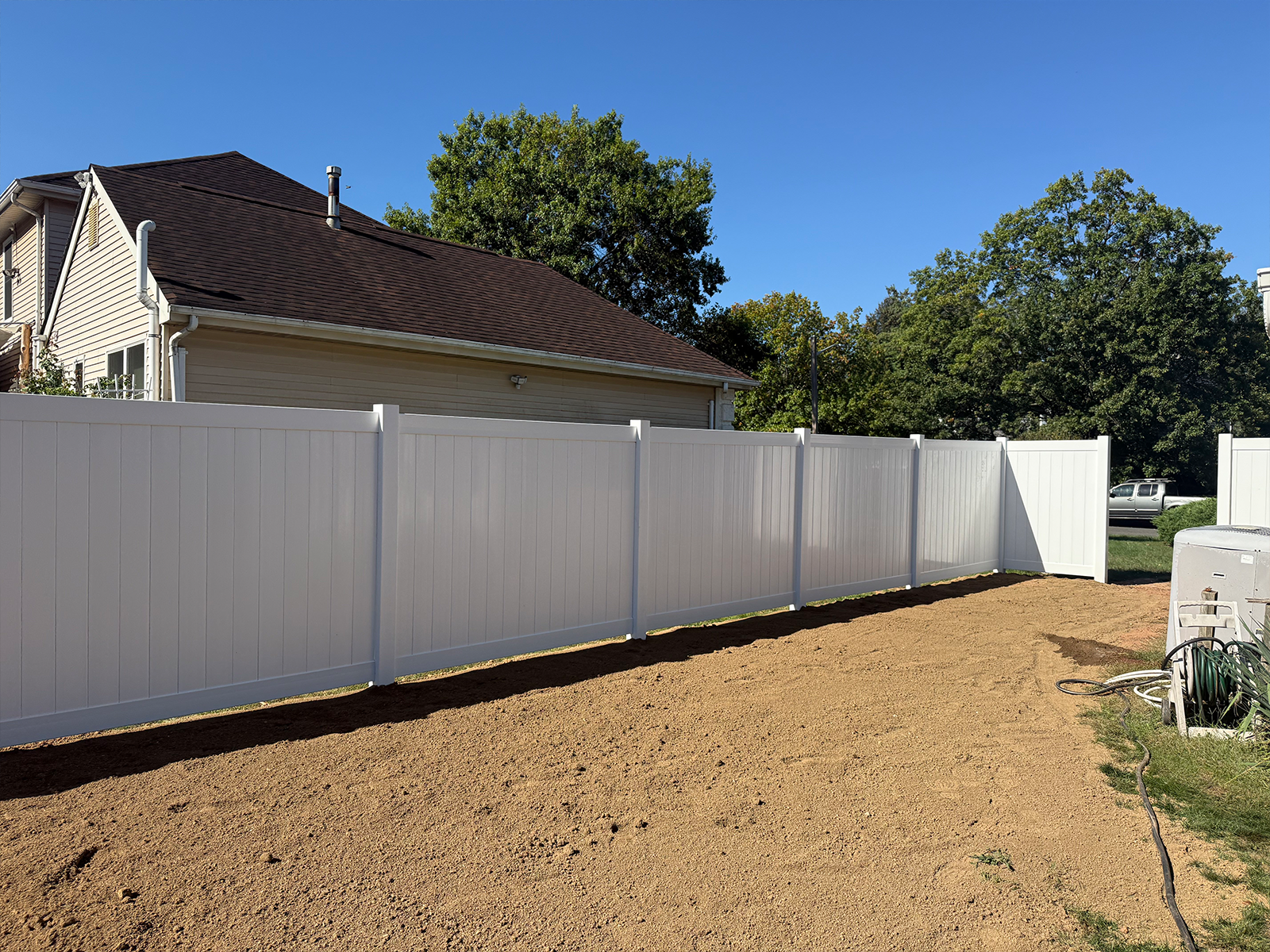 White vinyl fence installation in residential yard, enhancing privacy and property value, with a clear blue sky in the background.
