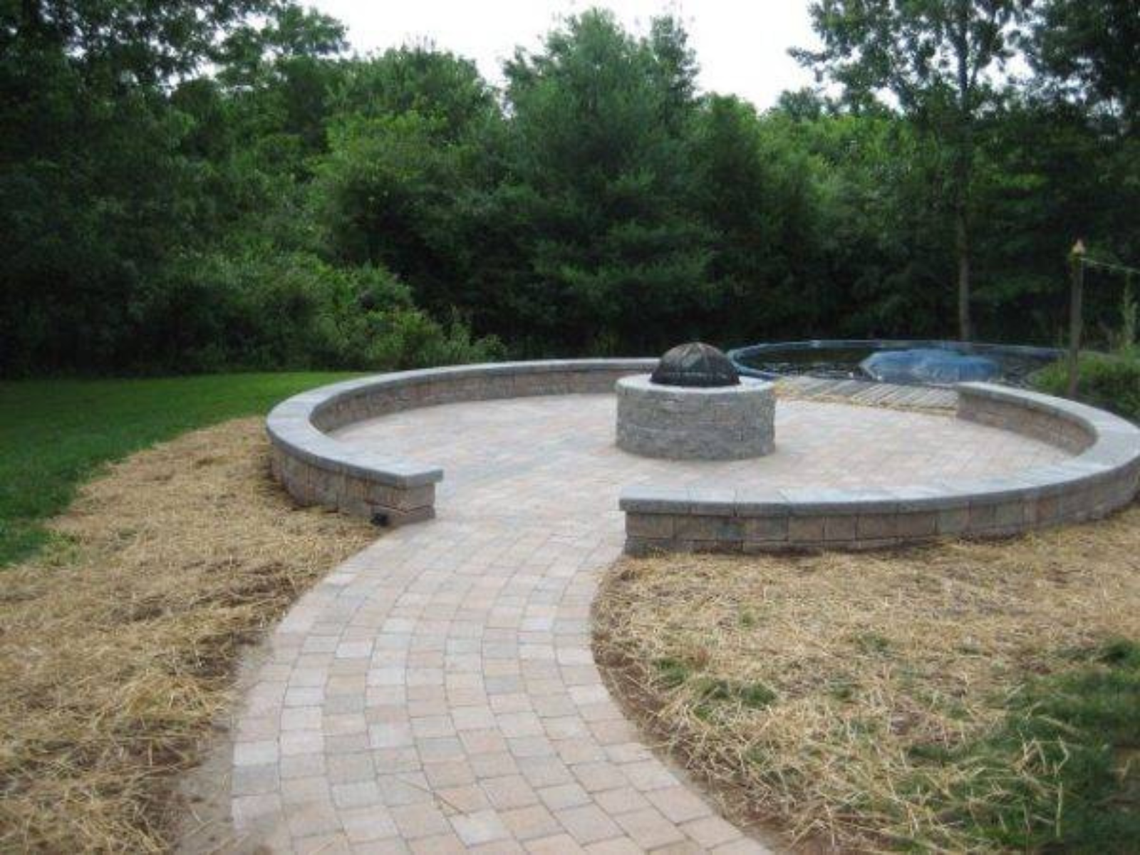 Patio with circular stone seating and fire pit, surrounded by lush greenery, designed for outdoor gatherings and relaxation in Princeton.