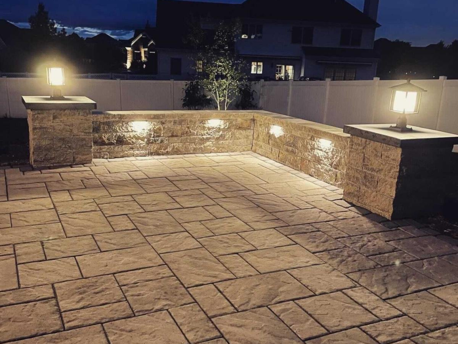 Patio area illuminated by landscape lighting, featuring stone walls and lantern-style fixtures, enhancing outdoor space usability and aesthetics in Princeton.