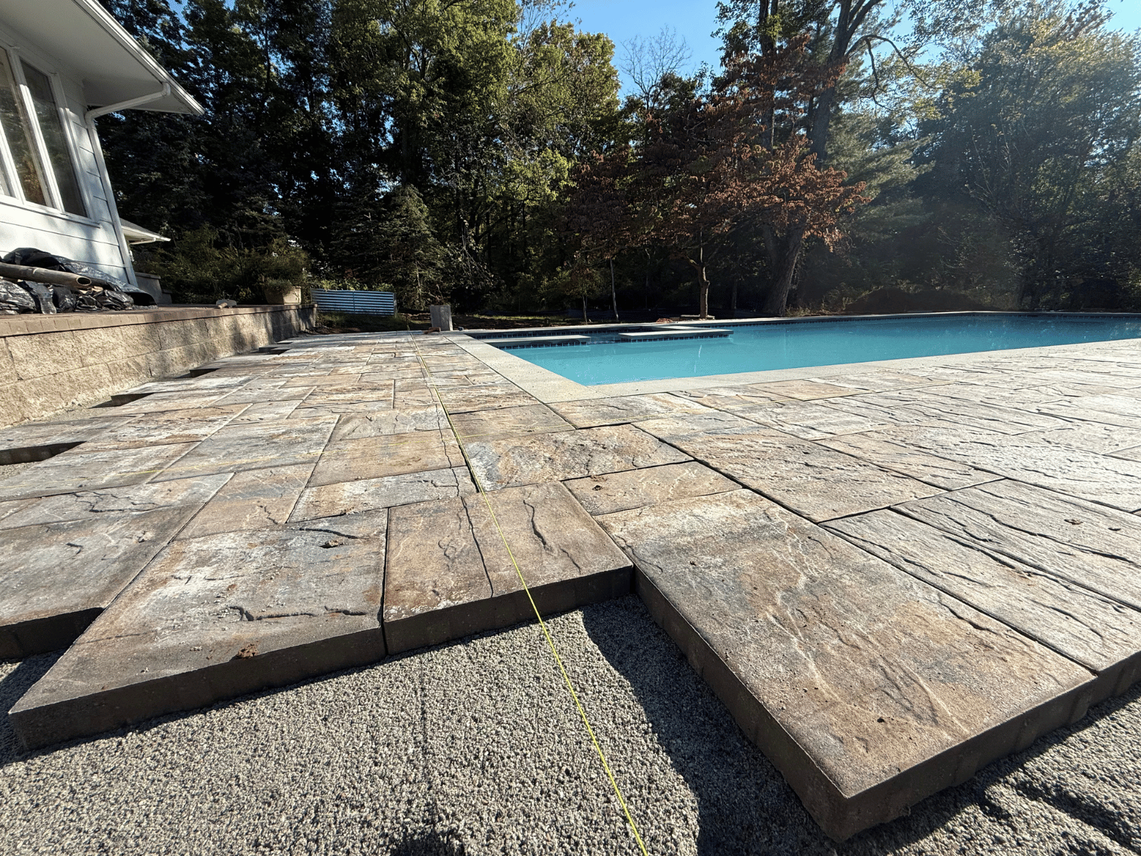 Swimming pool deck installation with textured stone pavers, surrounded by trees and a clear blue pool, showcasing Urban Landscape's landscaping expertise in Princeton, NJ.