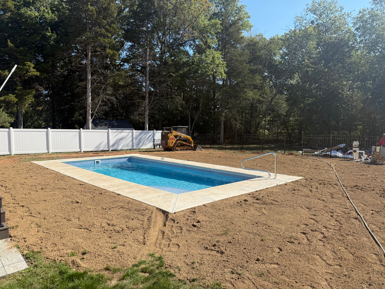pc Pool installation site in Princeton Township featuring a newly constructed swimming pool, surrounded by freshly graded earth and a white fence, with construction equipment visible in the background.