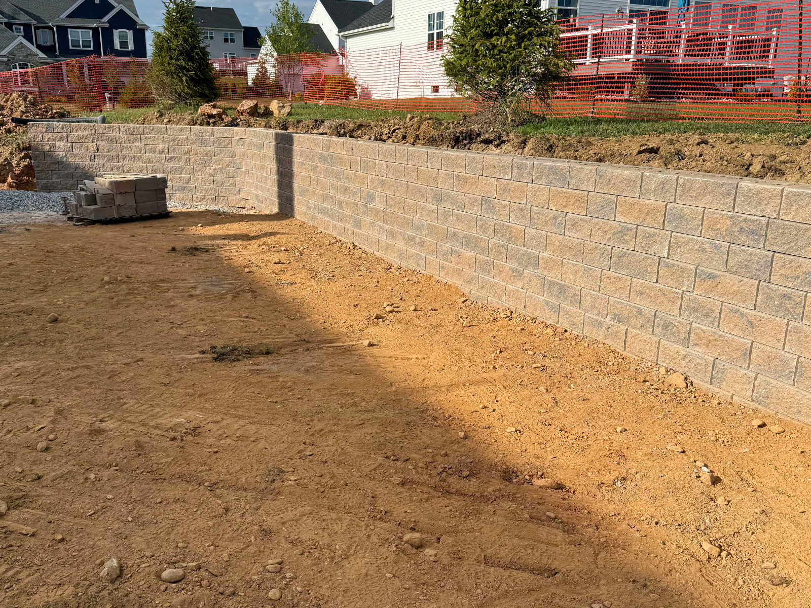 Retaining wall constructed with modern block systems, showcasing durable design and aesthetic appeal, surrounded by an unfinished landscape in a residential area.